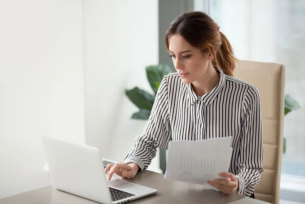 A businesswoman analyzing documents and working on a laptop, showcasing accounting and financial reporting services.