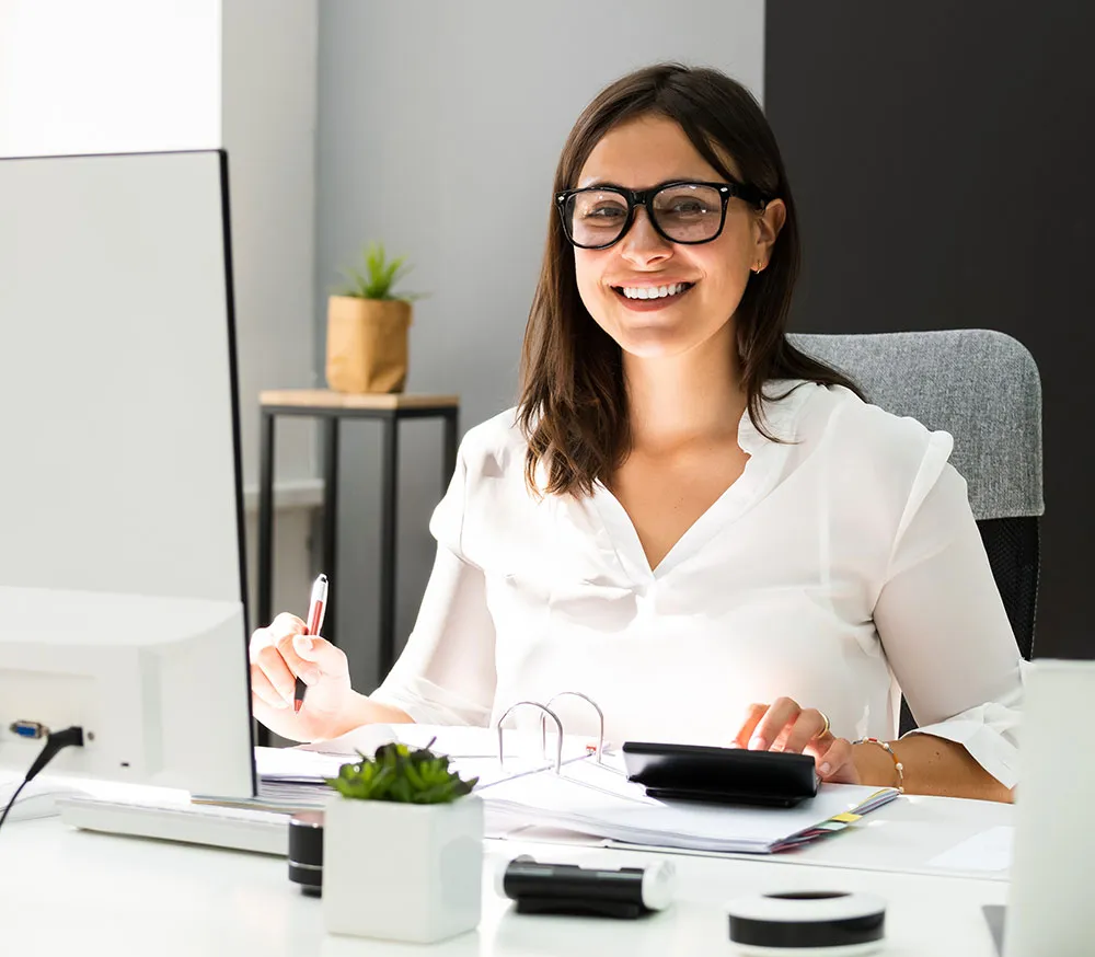 Smiling professional accountant working at her desk with a computer and calculator, providing bookkeeping services UAE