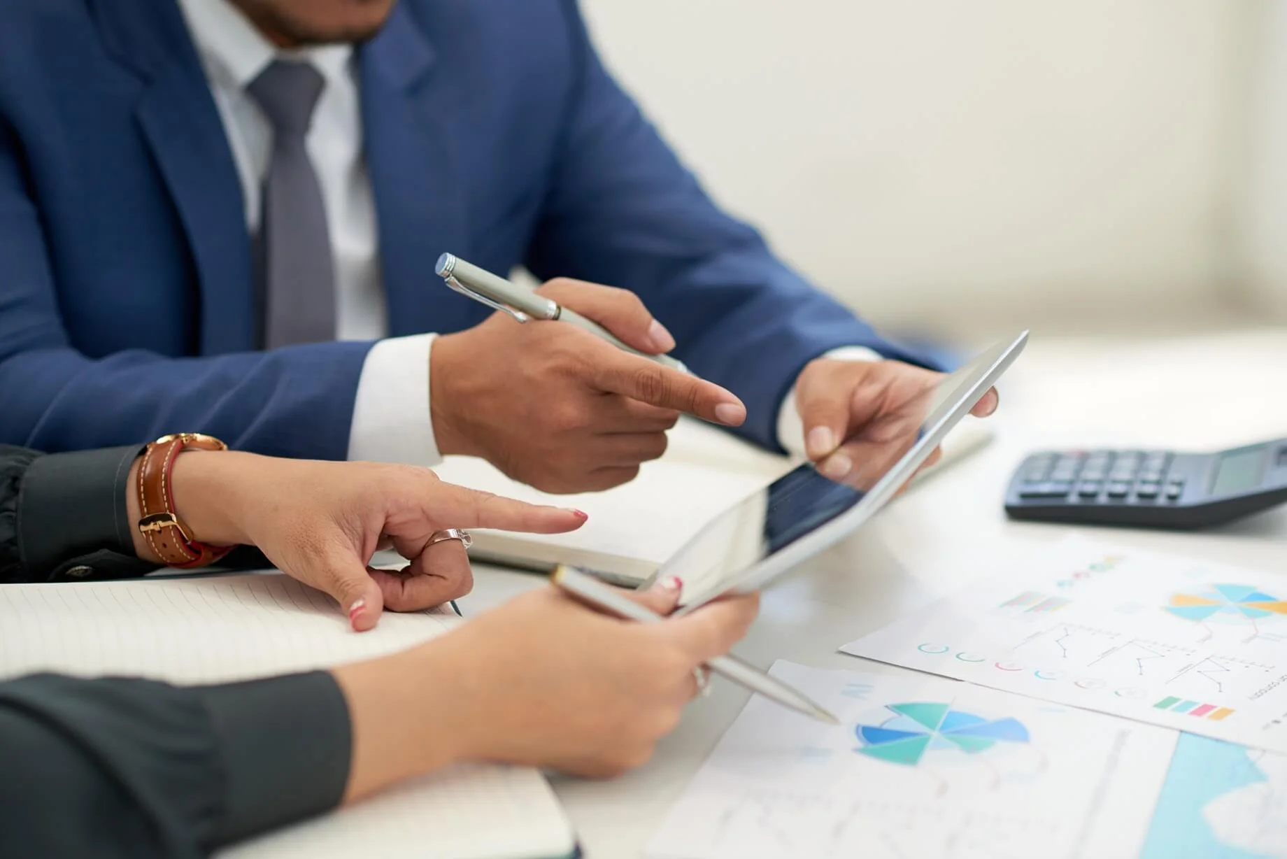 Unidentified business professionals in a meeting analyzing charts on a tablet.